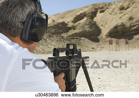 Stock Photograph - Man aiming machine gun at firing range. Fotosearch