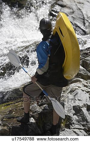 Stock Photo - Man carrying kayak, looking at river, back view. Fotosearch