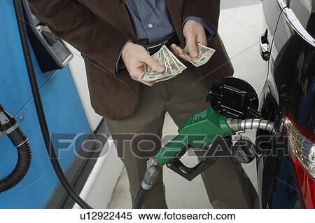 Stock Photography - Man counting money over gas pump in car, mid section. Fotosearch