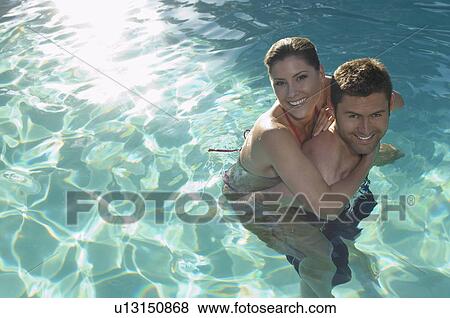 Stock Photo - Man giving woman piggy back in swimming pool, portrait. Fotosearch