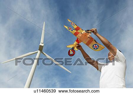 Stock Photo - Man holding airplane kite at wind farm. Fotosearch
