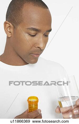 Stock Photo - Man holding bottle of pills and glass of water, studio shot. Fotosearch