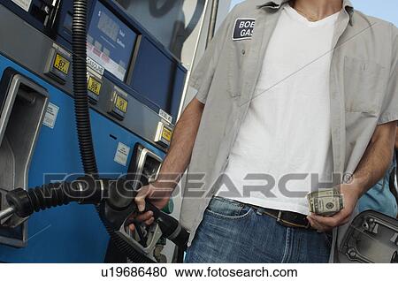 Stock Image - Man holding fuel pump and money, mid section. Fotosearch