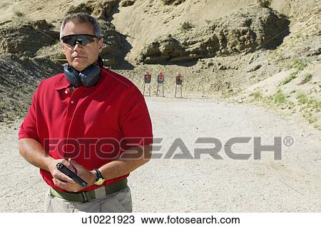Man holding hand gun at firing range, portrait View Large Photo Image Stock Image - Man holding hand gun at firing range, portrait. Fotosearch