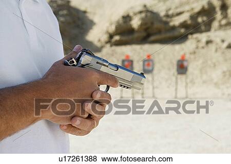 Man holding hand gun at firing range, mid section, close-up View Large Photo Image Stock Photo - Man holding hand gun at firing range, mid section, close-up. Fotosearch