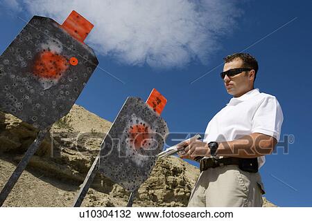 Man holding hand gun, near targets at firing range View Large Photo Image Stock Image - Man holding hand gun, near targets at firing range. Fotosearch