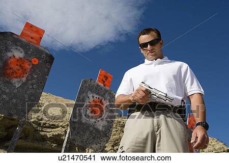 Man holding hand gun, near targets at firing range View Large Photo Image Stock Image - Man holding hand gun, near targets at firing range. Fotosearch