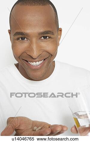 Stock Photography - Man holding pills and glass of water, portrait. Fotosearch