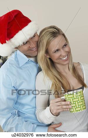 Stock Photograph - Man in Santa hat with arm around woman with coffee cup. Fotosearch