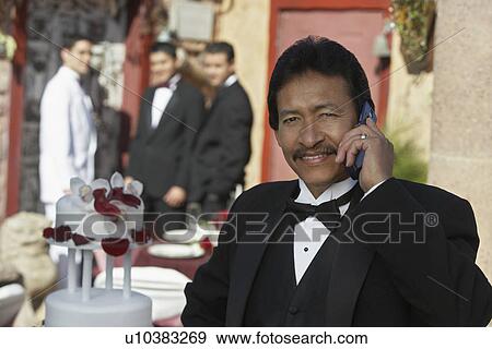 Stock Photo - Man in tuxedo at Quinceanera, using mobile phone. Fotosearch