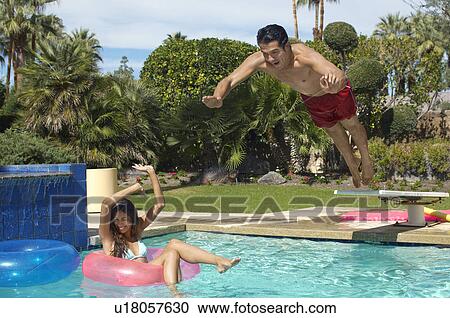 Man jumping into swimming pool over woman on inflatable raft View Large Photo Image Stock Image - Man jumping into swimming pool over woman on inflatable raft. Fotosearch