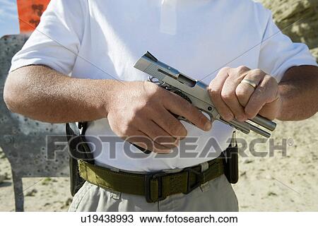 Stock Image - Man loading hand gun at firing range, mid section. Fotosearch
