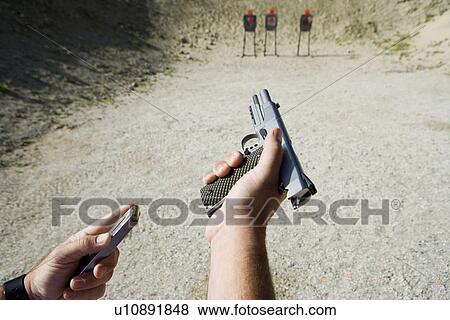 Stock Photo - Man loading hand gun at firing range, focus on hands. Fotosearch