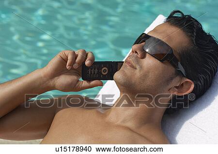 Man lying on sunlounger and talking on mobile phone, close-up View Large Photo Image Stock Image - Man lying on sunlounger and talking on mobile phone, close-up. Fotosearch