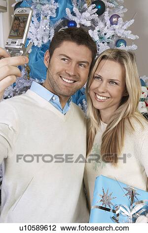 Man photographing self and woman with cell phone in front of Christmas tree View Large Photo Image Stock Image - Man photographing self and woman with cell phone in front of Christmas tree. Fotosearch