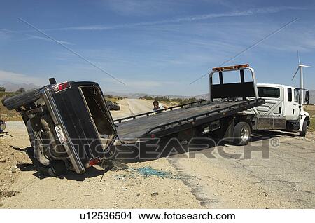 Picture - Man preparing to lift crashed car onto tow truck. Fotosearch