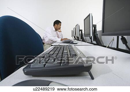 Man sitting at desk in front of computer View Large Photo Image Stock Photo - Man sitting at desk in front of computer. Fotosearch