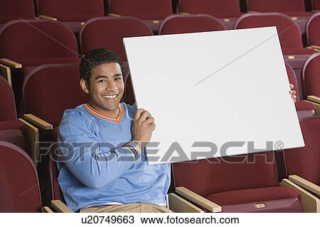 Stock Image - Man sitting in auditorium, holding empty placard. Fotosearch