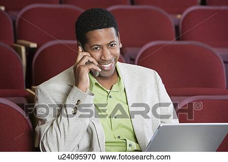 Man sitting in auditorium, using mobile phone and laptop, portrait View Large Photo Image Stock Image - Man sitting in auditorium, using mobile phone and laptop, portrait. Fotosearch
