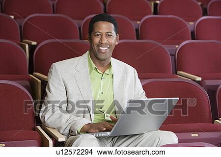 Man sitting in auditorium with laptop, portrait View Large Photo Image Picture - Man sitting in auditorium with laptop, portrait. Fotosearch