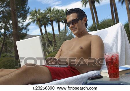 Stock Image - Man sitting on deckchair, using laptop. Fotosearch