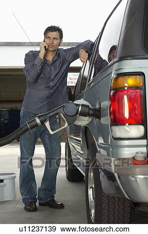 Stock Photo - Man using cell phone leaning on van with fuel pump. Fotosearch