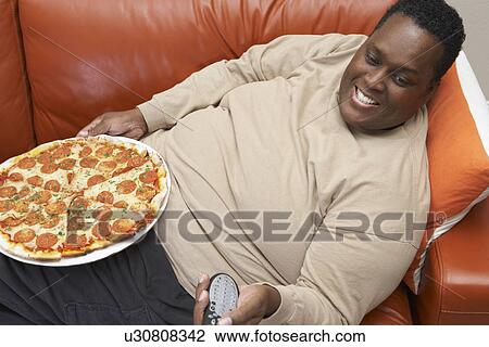 Stock Image - Man watching tv with pizza on lap. Fotosearch