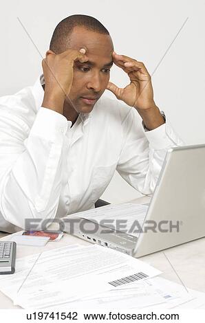 Stock Image - Man with a Laptop Figuring out Bills. Fotosearch