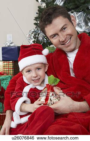 Stock Photograph - Man with arm around boy (5-6) in Santa hat holding Christmas present. Fotosearch