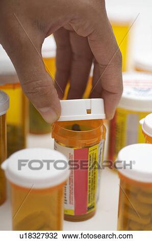 Stock Image - Man's hand opening pill bottle, close-up. Fotosearch