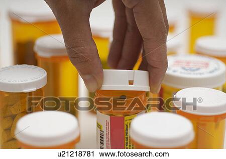 Stock Image - Man's hand opening pill bottle, close-up. Fotosearch