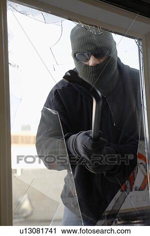 Stock Image - Masked thief braking glass with crowbar. Fotosearch