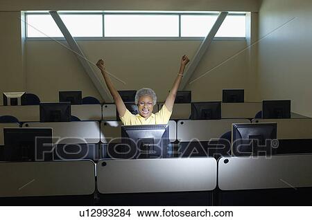 Picture - Mature female student celebrating in computer classroom. Fotosearch