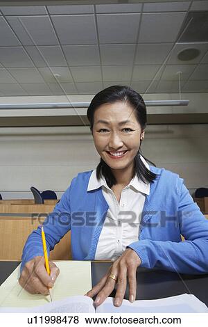 Stock Photo - Mature female student working in lecture theatre, portrait. Fotosearch