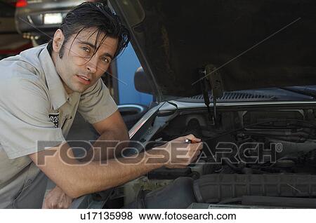 Stock Photo - Mechanic pointing at engine, portrait. Fotosearch