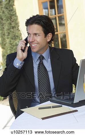 Stock Image - Mid adult business man talking on mobile in cafe. Fotosearch