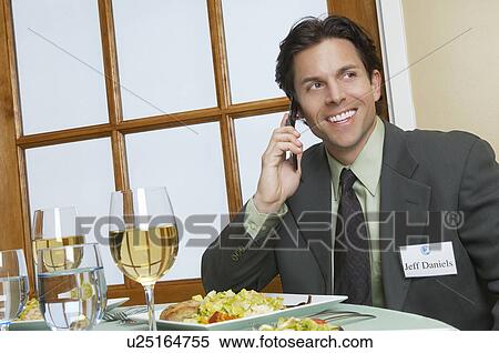 Stock Photography - Mid adult business man talking on mobile at restaurant table. Fotosearch