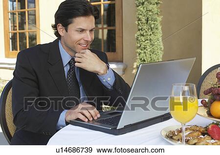 Mid adult business man working on laptop at outdoor cafe table View Large Photo Image Stock Photo - Mid adult business man working on laptop at outdoor cafe table. Fotosearch