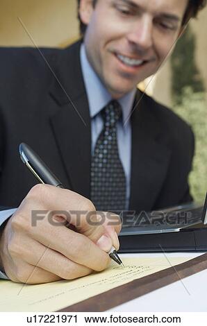 Stock Image - Mid adult business man writing, focus on foreground. Fotosearch