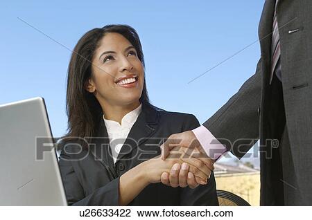 Stock Image - Mid adult business woman in front of laptop shaking hands with man (mid section). Fotosearch
