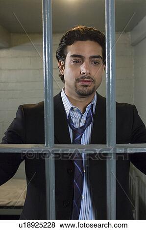Mid-adult businessman standing behind cell bars View Large Photo Image Stock Photo - Mid-adult businessman standing behind cell bars. Fotosearch