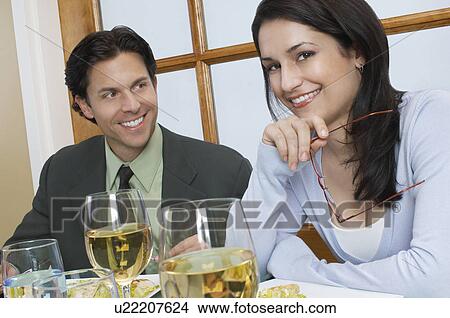Picture - Mid adult couple at restaurant table, woman looking at camera. Fotosearch