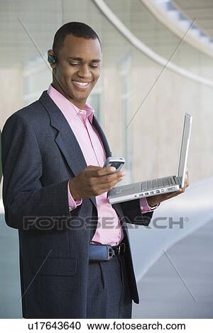 Stock Image - Mid adult man using laptop and PDA outdoors. Fotosearch