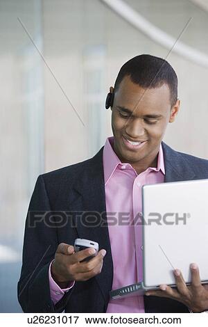 Stock Photo - Mid adult man using laptop and PDA outdoors. Fotosearch