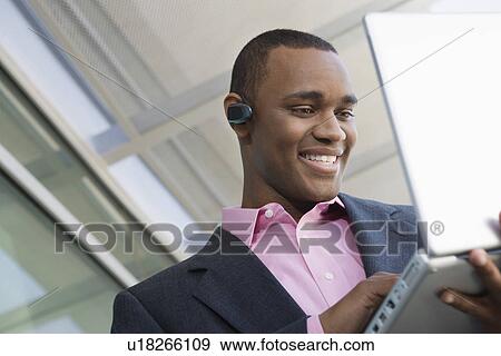 Stock Photo - Mid adult man using laptop outdoors. Fotosearch