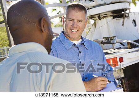 Stock Photo - Mid-adult mechanic talking to co-worker. Fotosearch