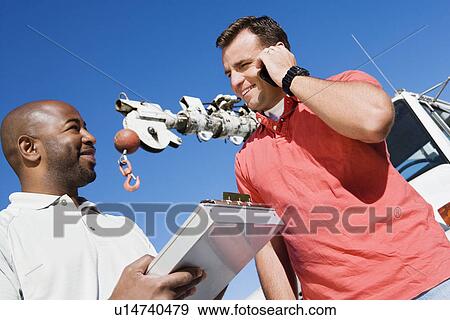 Stock Photo - Mid-adult mechanic talking with co-worker. Fotosearch