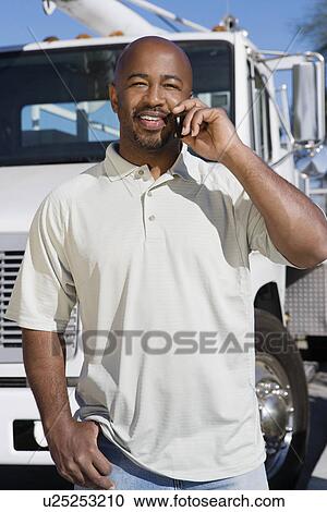 Stock Image - Mid-adult truck driver on the phone in front of a truck. Fotosearch