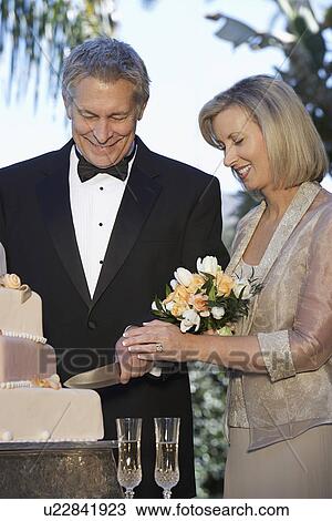 Stock Image - Middle-aged couple cutting wedding cake, portrait. Fotosearch