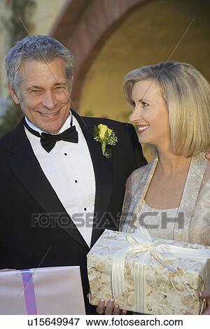 Stock Photo - Middle-aged couple in formal wear holding presents, portrait. Fotosearch